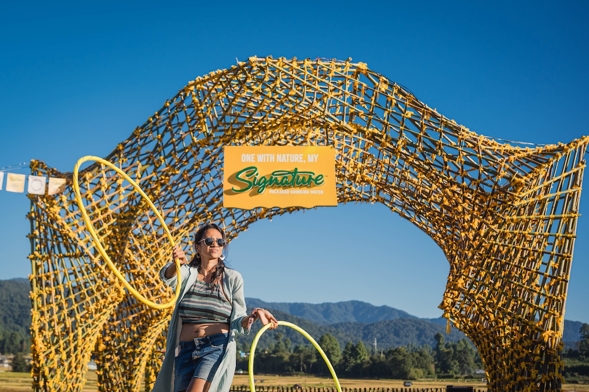 The image shows a facilitator leading the Signature Masterclass on Flow State of Mind by Signature Packaged Drinking Water at the Ziro Festival, combining awareness frameworks, hula hooping, Capoeira, and grounding rituals.